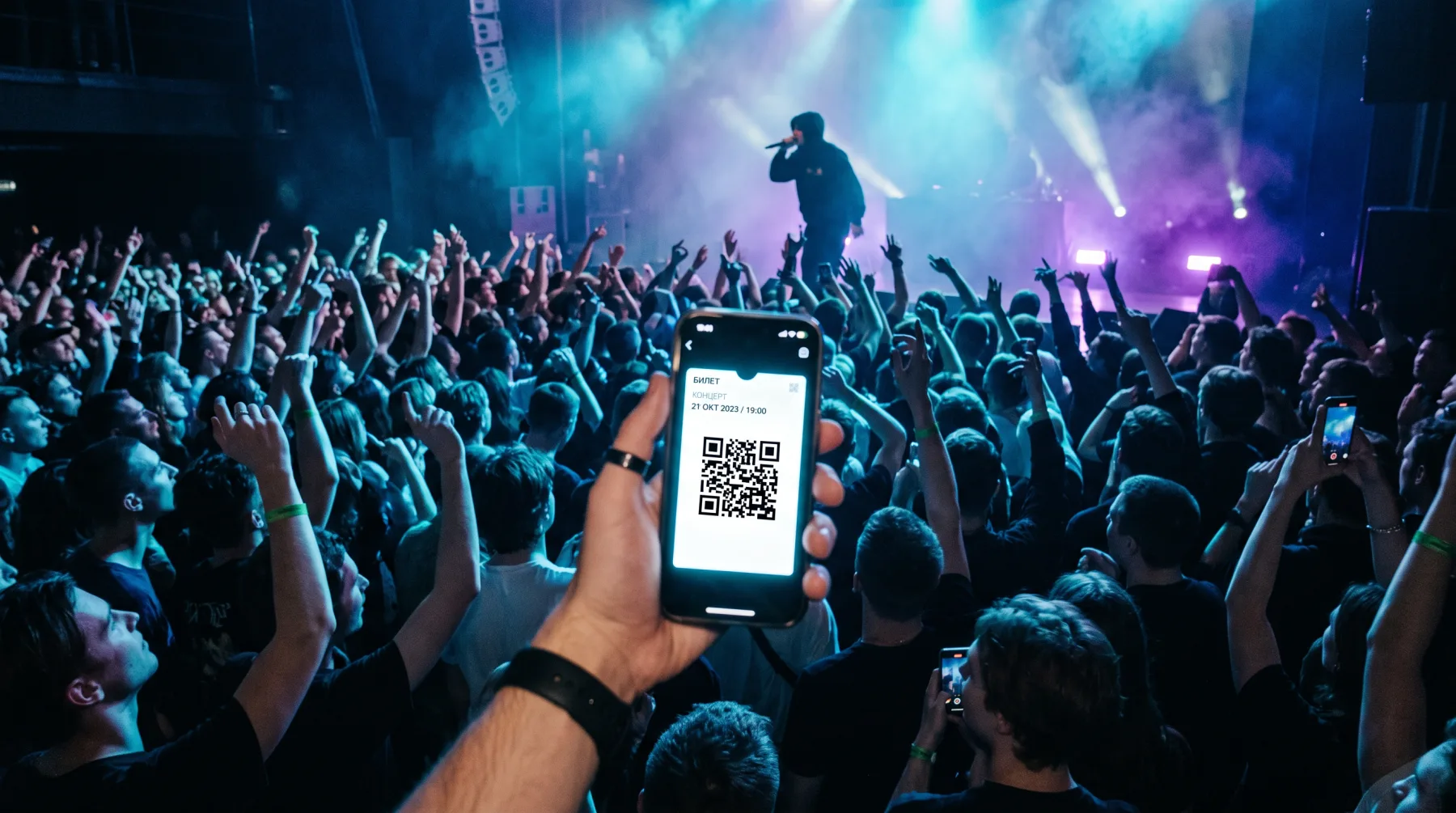 Полный зал на концерте, гость показывает билет с QR-кодом на телефоне